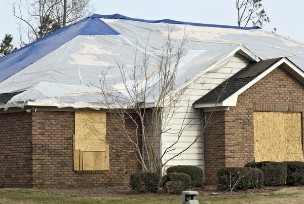 Brick Home with tarped roof from storm damage and boarded windows-1