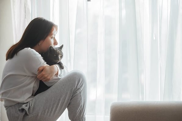 Concerned girl holding cat looking out window
