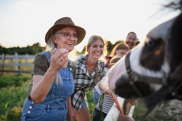 Generation family with grandmom, adult daughter, and children feeding horse carrots over fence