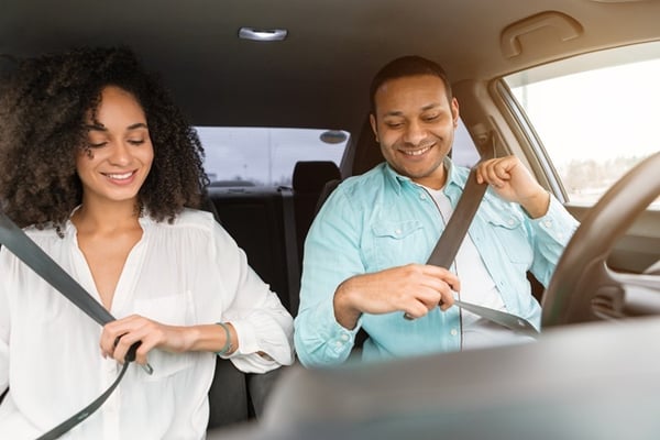 black smiling woman and man putting on seatbelt