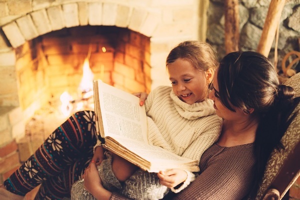 happy mom with girl child reading book together by fireplace-1