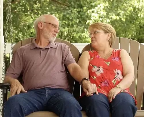 older couple sitting together on home porch swing and smiling at each other
