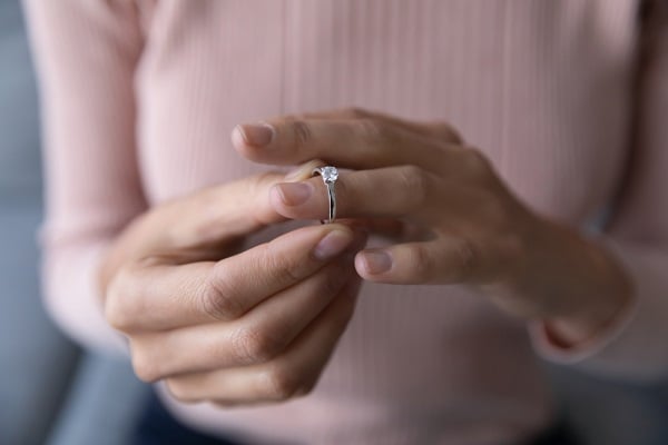 Woman in pink sweater putting engagement ring on finger